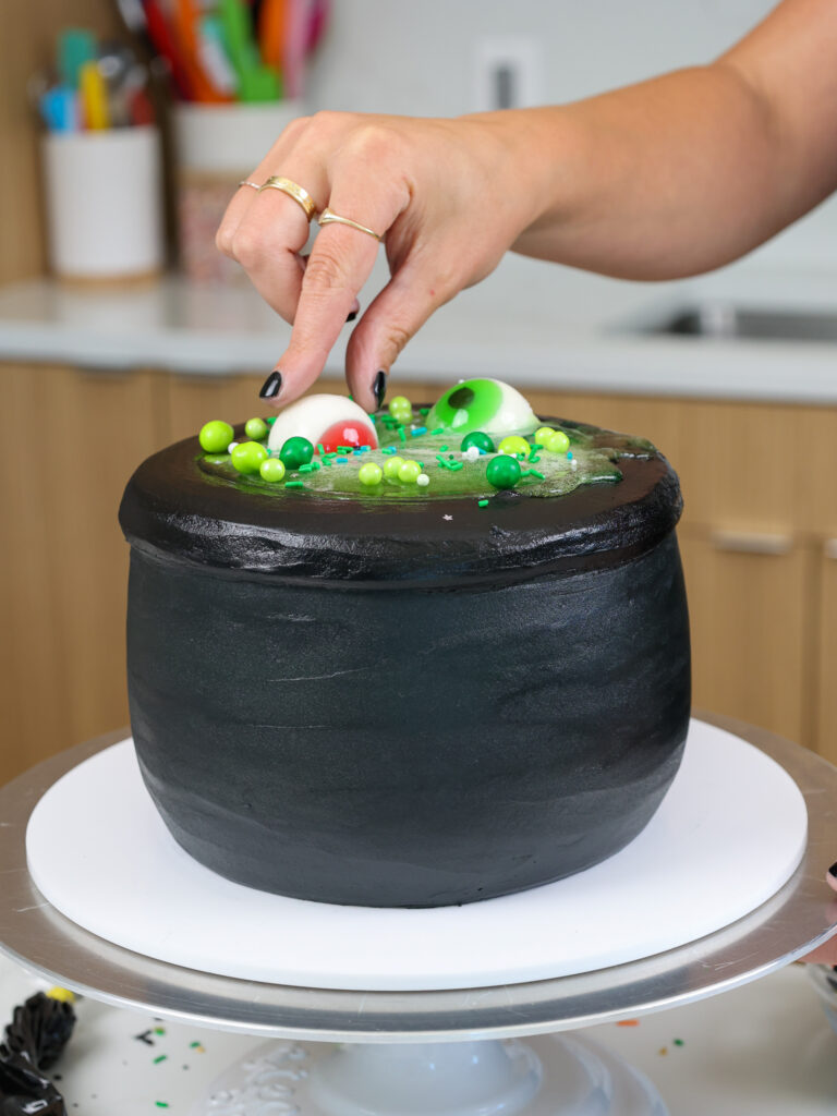 image of gummy eyeballs being added to the top of a spooky halloween cauldron cake