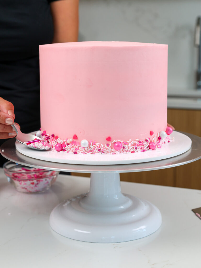 image of pink sprinkles being added to the base of a pink cake