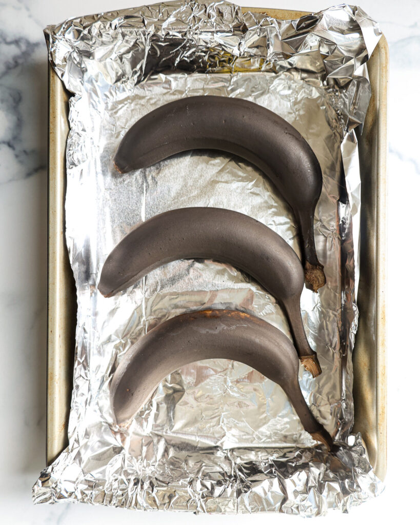 image of unripe bananas that have been placed on a foil lined baking sheet to be quickly ripened by being baked the oven