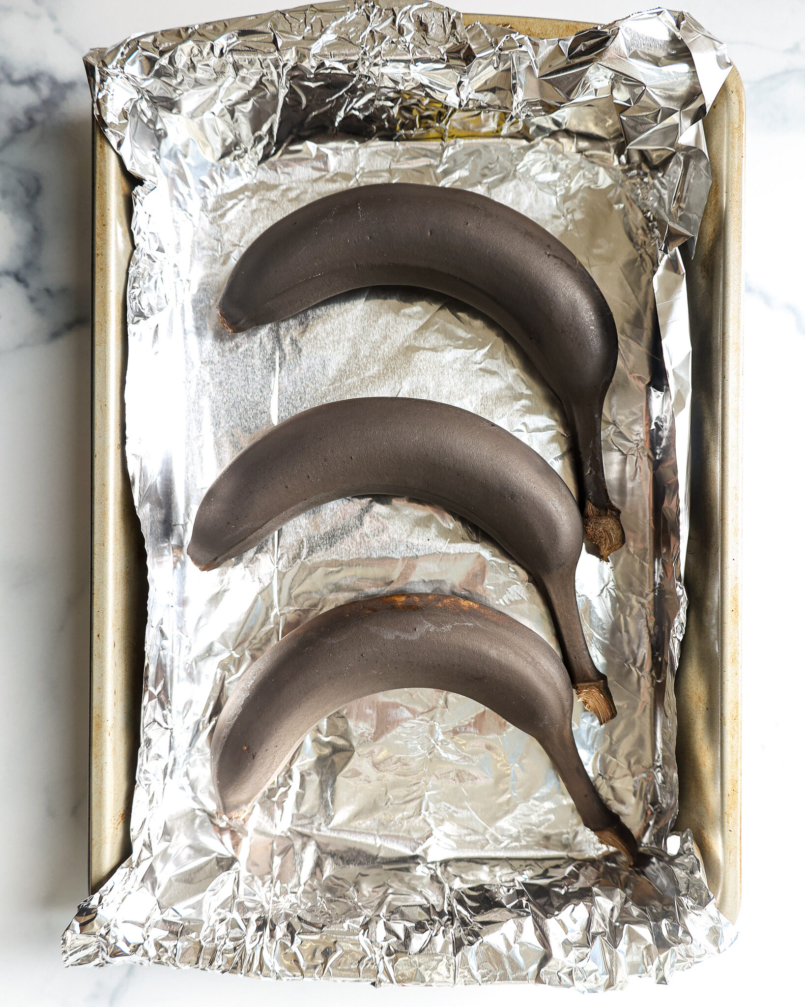 image of unripe bananas that have been placed on a foil lined baking sheet to be quickly ripened by being baked the oven