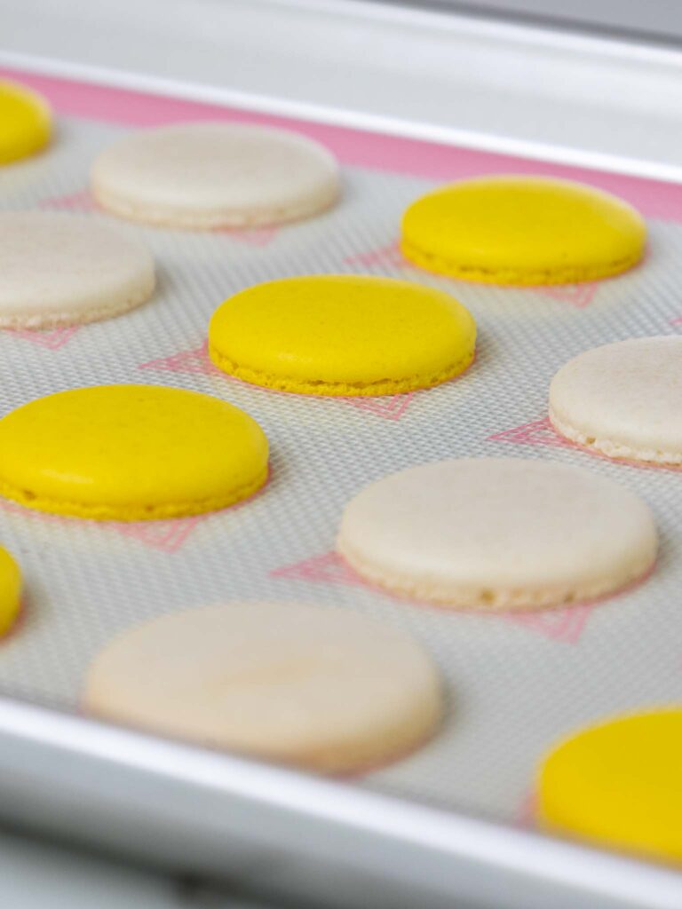 image of baked yellow and white french macaron shells cooling on a silpat mat
