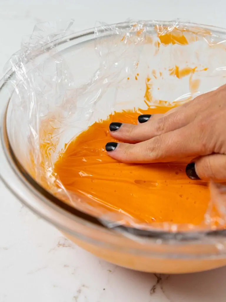 image of candy corn ganache being covered flush with plastic wrap before being chilled in the fridge for a few hours