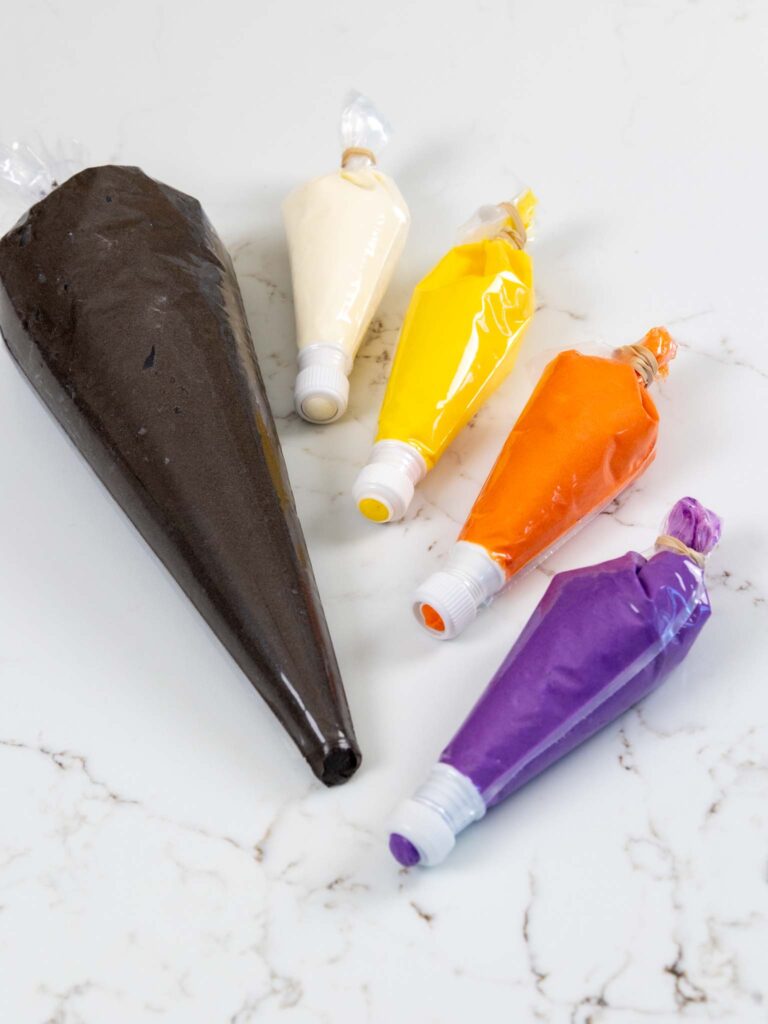 image of black, white, yellow, orange, and purple American buttercream that have been put in piping bags to decorate a cake