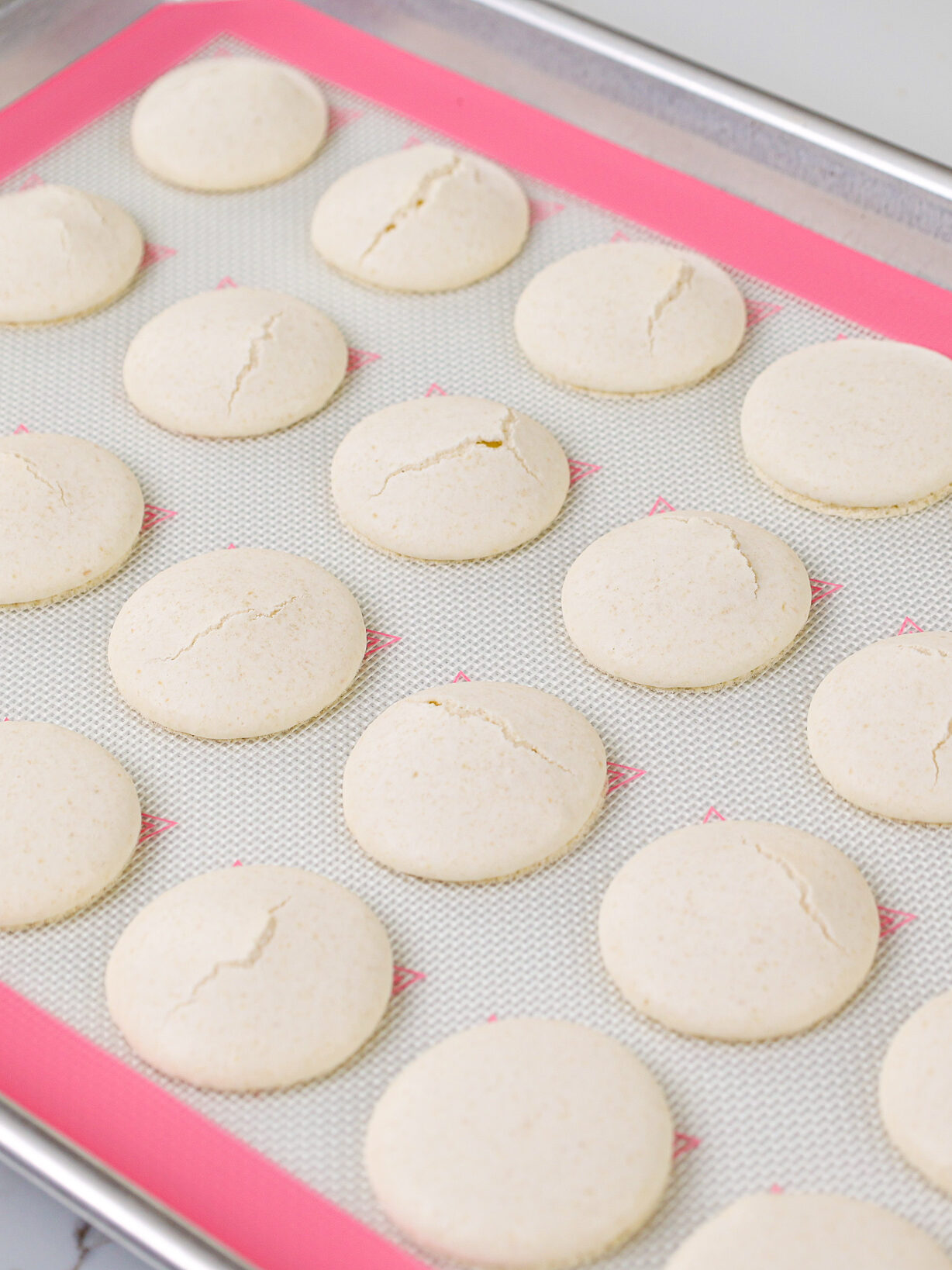 image of white macaron shells that have cracked because the oven was too hot