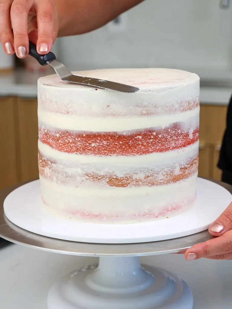 image of a cake that's being crumb coated with vanilla buttercream