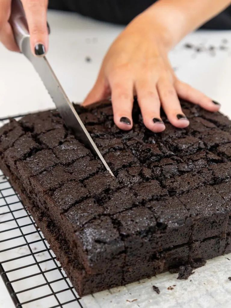 image of a square chocolate sheet cake being cut into small cubes with a serrated knife