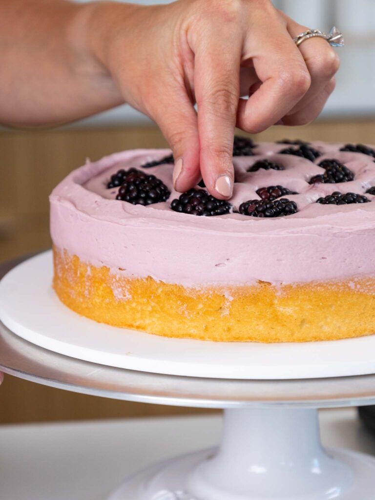 image of blackberries being pressed into blackberry mousse cake filling as a layer cake is being stacked