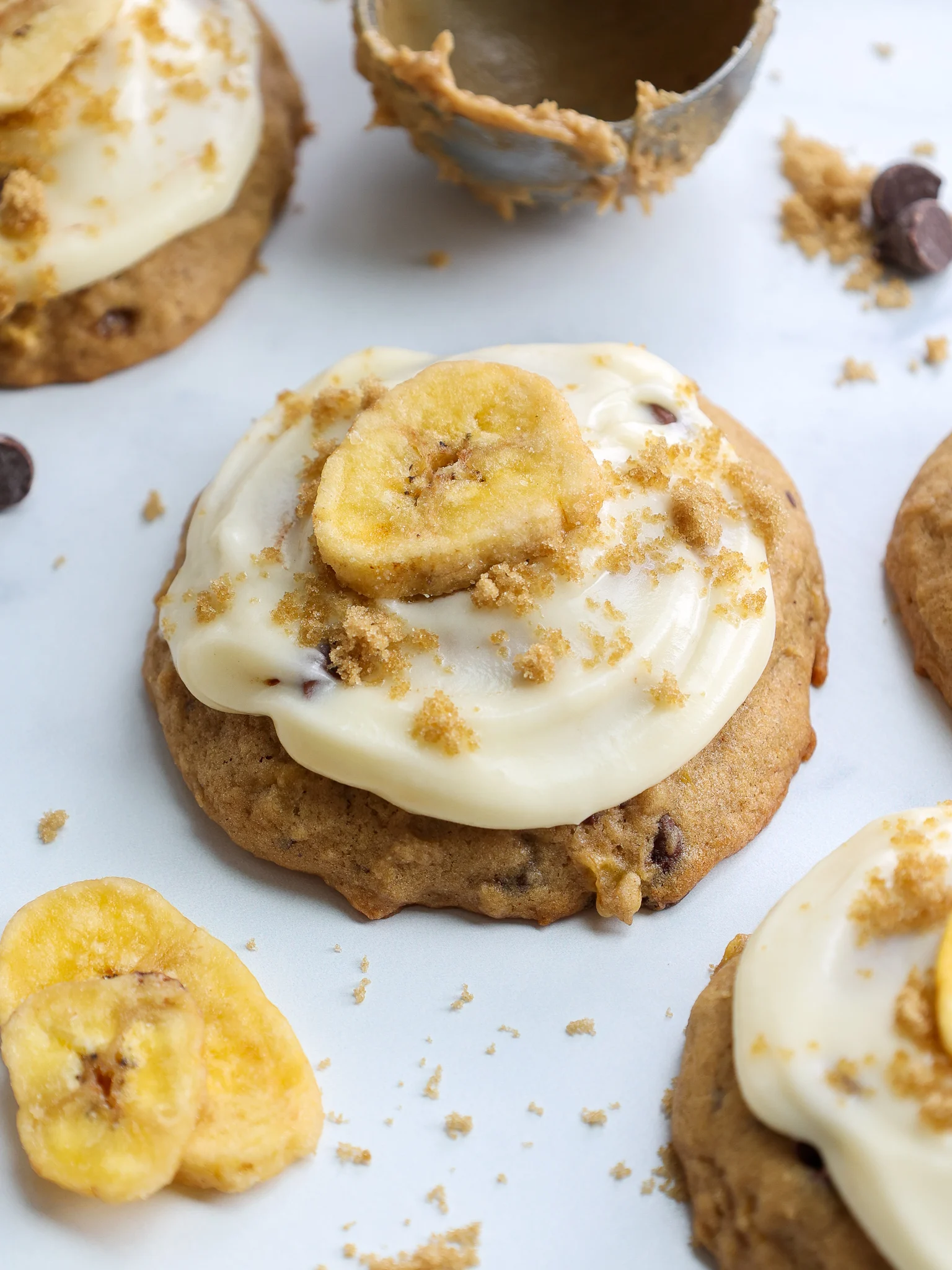 image of soft banana cookies that have been frosted with cream cheese frosting and topped with a banana chip