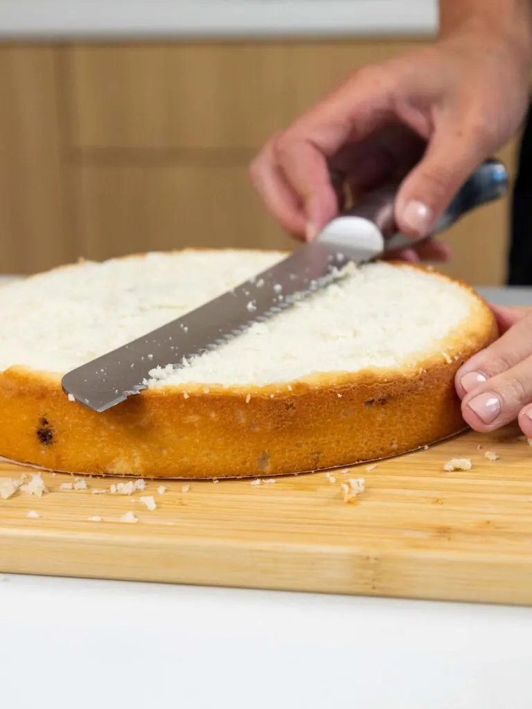 image of a vanilla blackberry swirled vanilla cake layer being leveled with a serrated knife