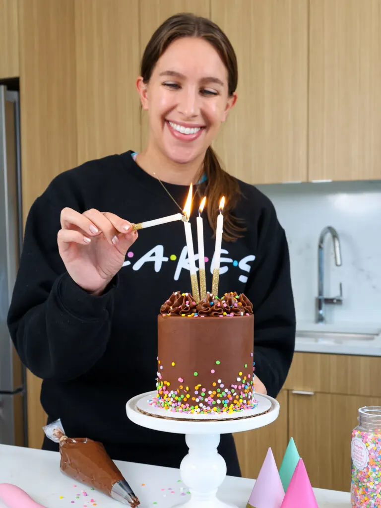 image of chelsey white of chelsweets lighting candles on a small chocolate smash cake