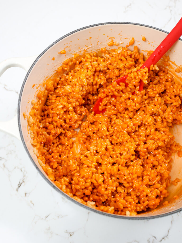 image of pumpkin rice kripsies being mixed together in a large pot with pumpkin spice and orange gel food coloring 