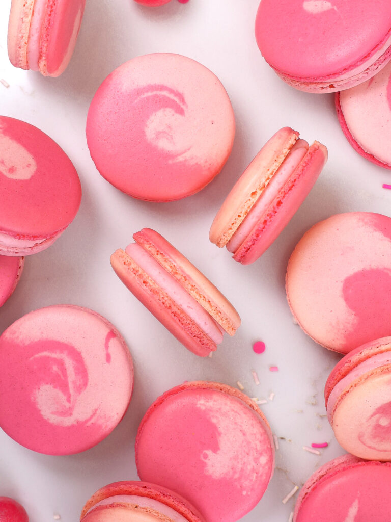 image of bubblegum macarons laid out on a counter to show their two toned pink shells and bubblegum frosting filling