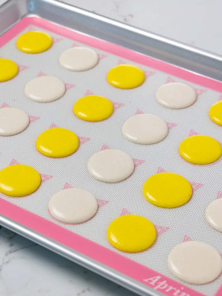 image of yellow and white macaron shells that have been piped on a silpat mat and are resting before being baked