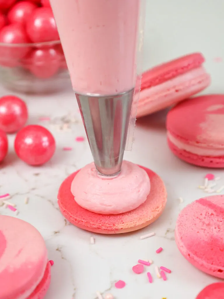 image of a pink macaron shell being filled with bubblegum frosting