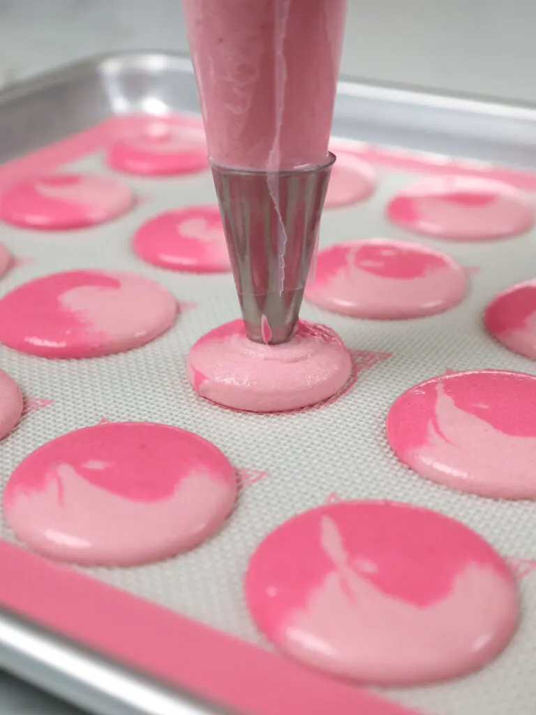 image of two-toned pink macaron shells being piped