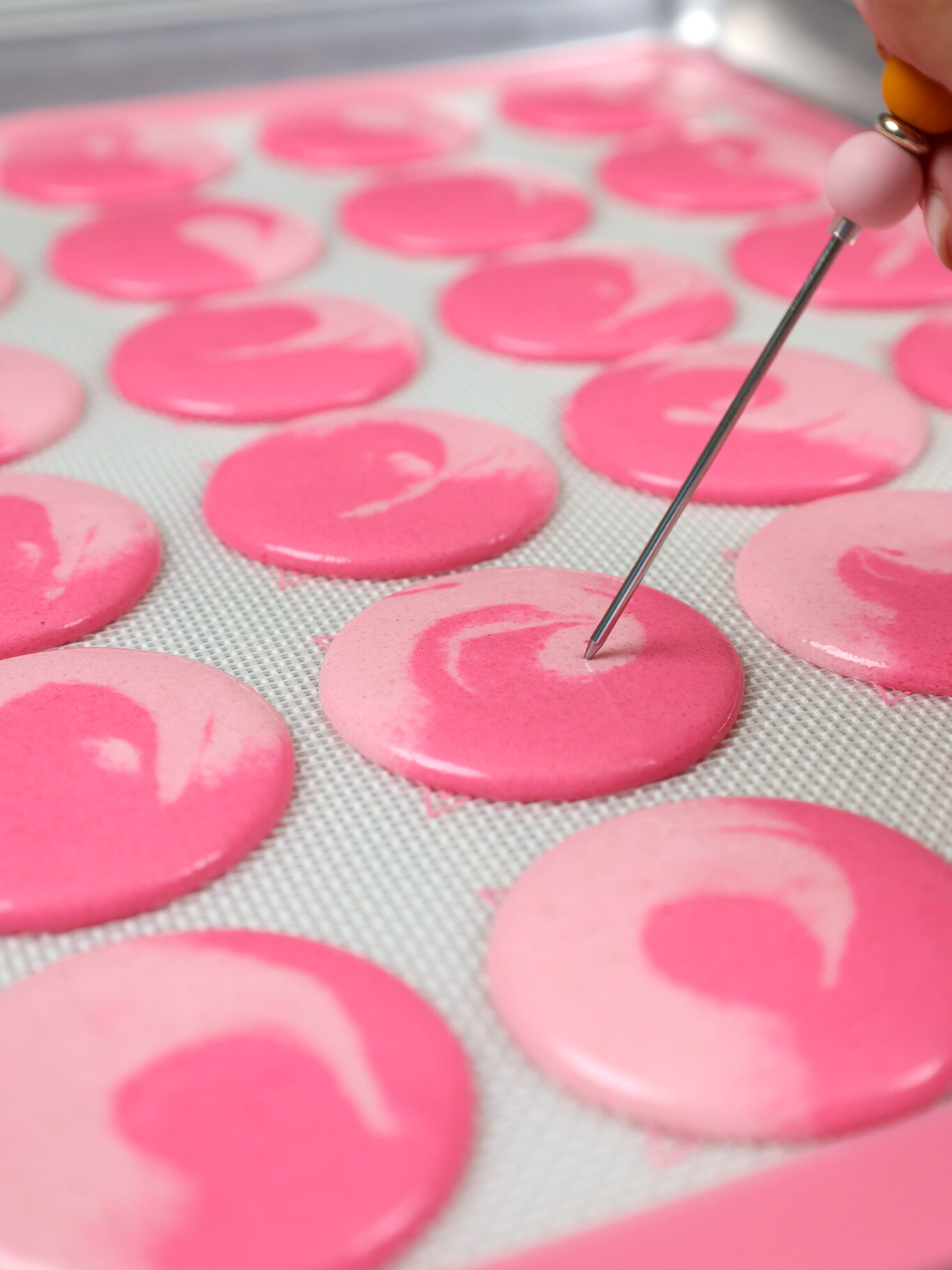 image of bubbles being popped in a two-toned pink macaron shell before being rested