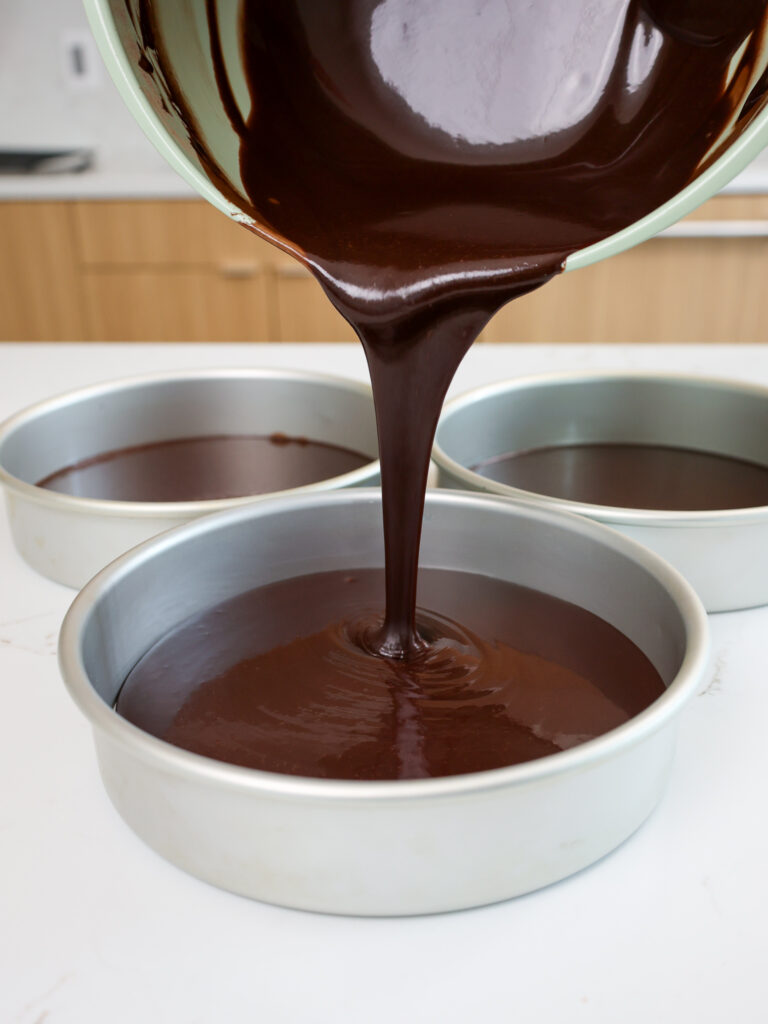 image of chocolate cake batter being poured into 8 inch cake pans