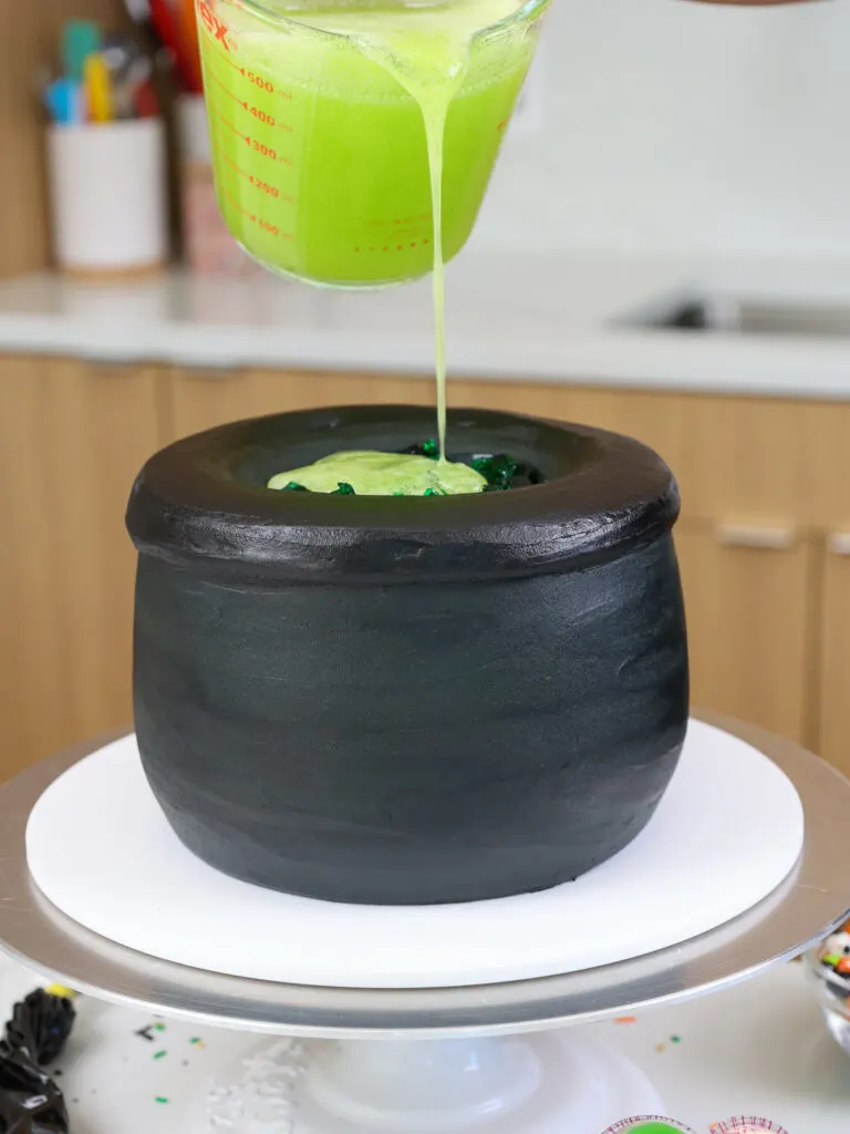 image of lime green gelatin being poured into the center of a cauldron cake