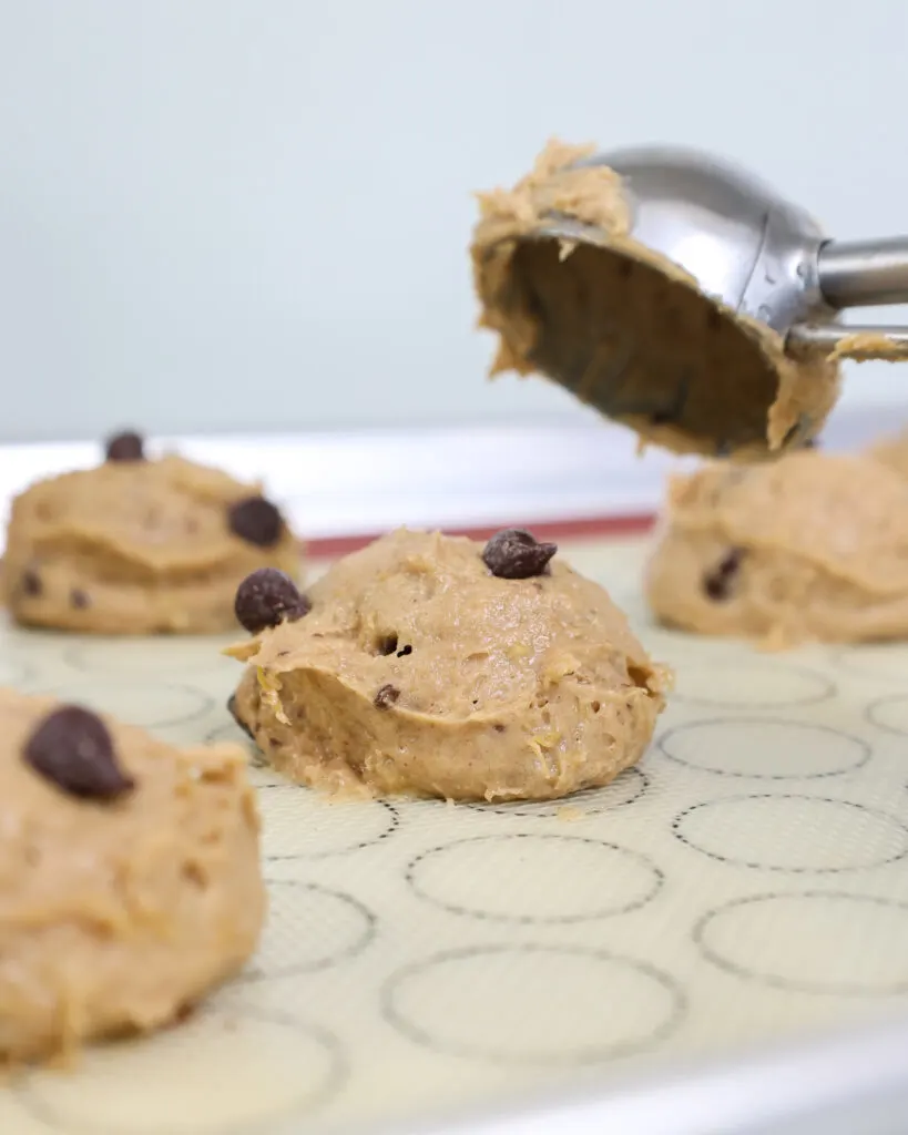 image of banana cookie batter being scooped on a baking sheet with a cookie scoop