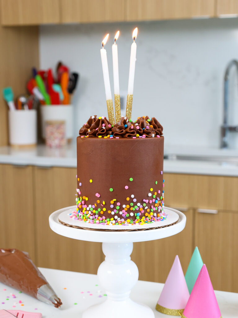 image of a 4-inch chocolate smash cake that's been decorated with small round sprinkles and tall candles

