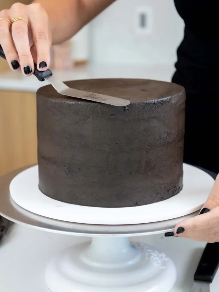 image of a black cocoa cake being crumb coated with a thin layer of dark chocolate frosting