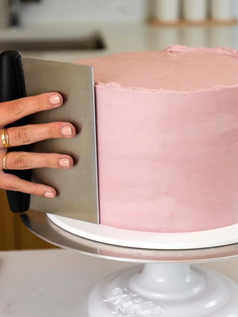 image of blackberry buttercream being smoothed onto a blackberry mousse cake with a bench scraper