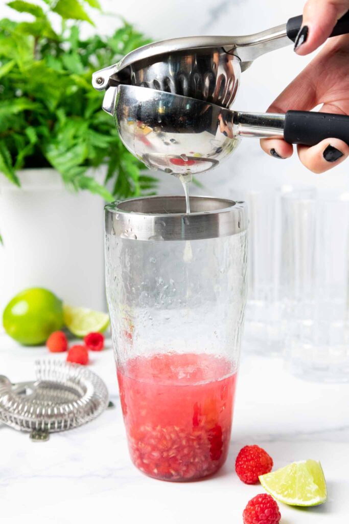 image of lime juice being squeezed into a cocktail shaker to make a raspberry gin cocktail