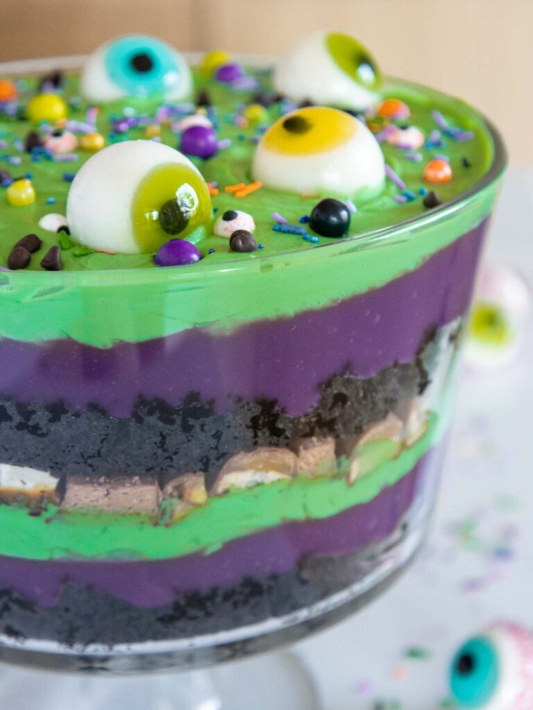 image of a halloween trifle made with purple and green pudding and whipped cream and decorated with gummy eyeballs and halloween sprinkles