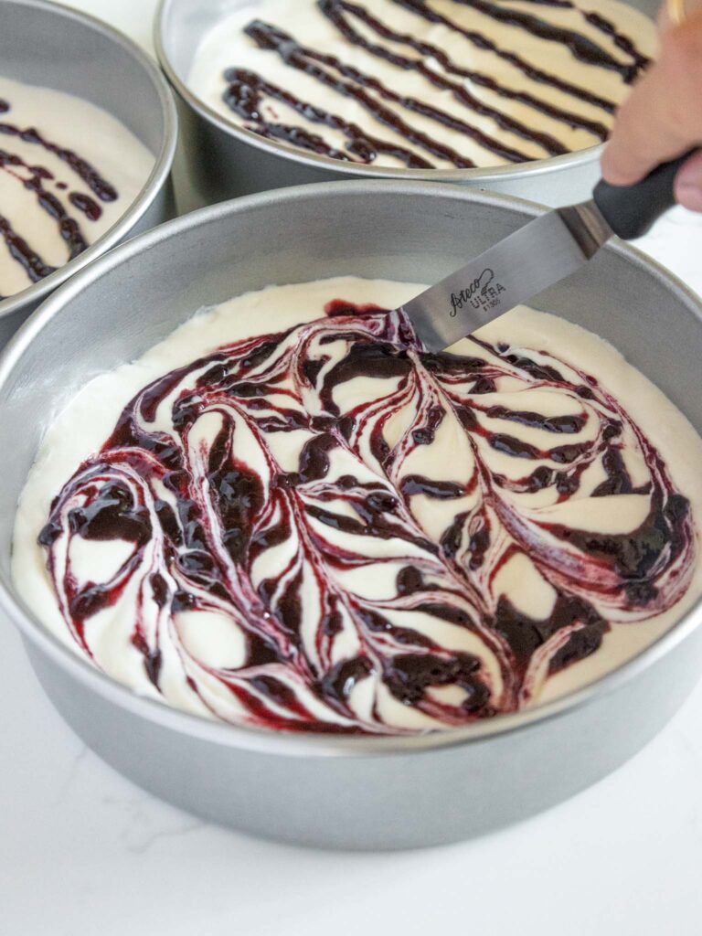 image of blackberry jam being swirled into vanilla cake batter to make blackberry swirled cake layers for a blackberry mousse cake
