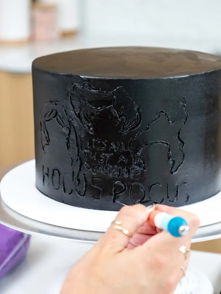image of a cake design being traced onto a black buttercream cake before piping on the buttercream decorations