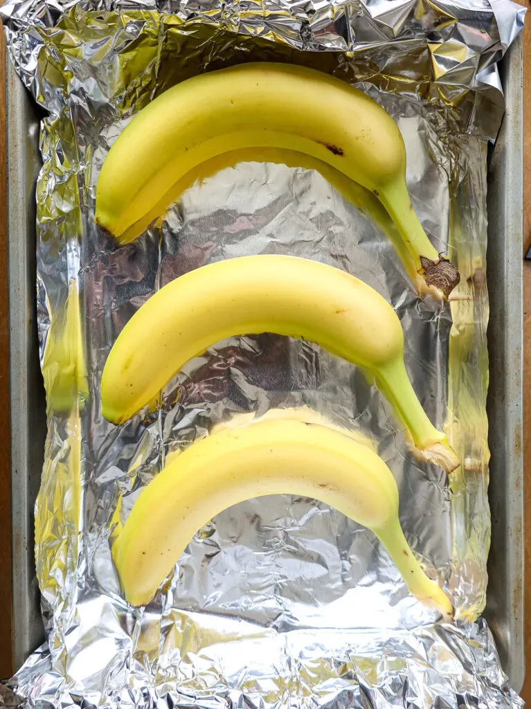 image of unripe bananas that have been placed on a foil lined baking sheet to be quickly ripened in the oven