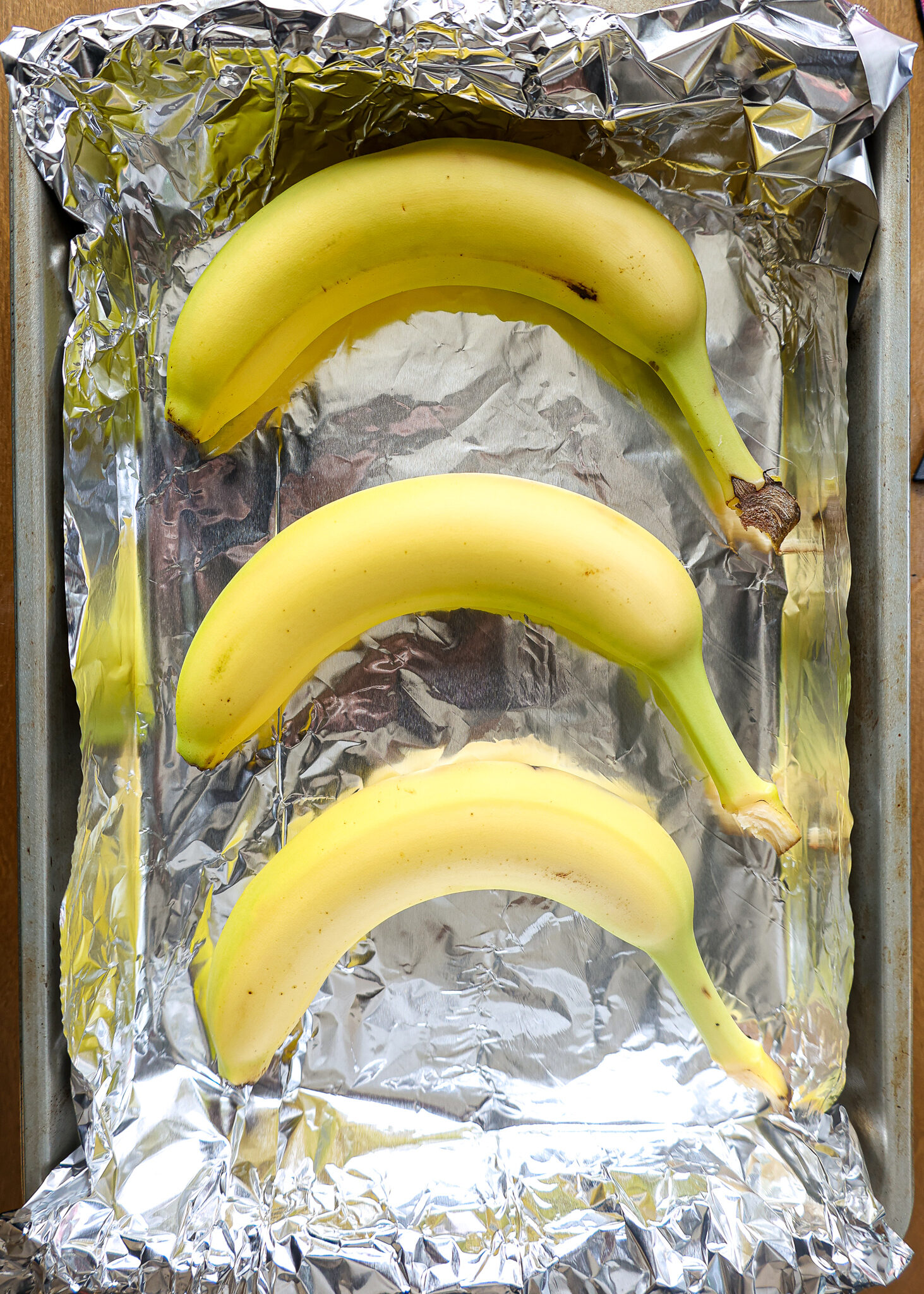 image of unripe bananas that have been placed on a foil lined baking sheet to be quickly ripened in the oven