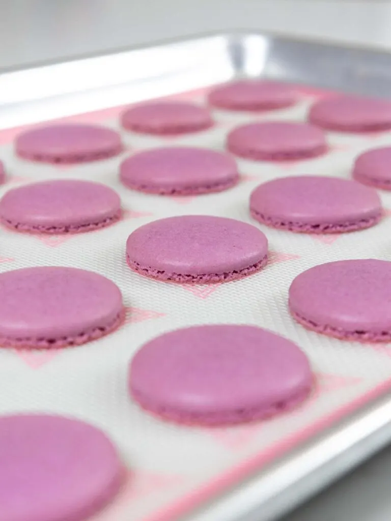 image of baked purple french macaron shells that have perfect feet and are cooling before being removed from the silpat mat