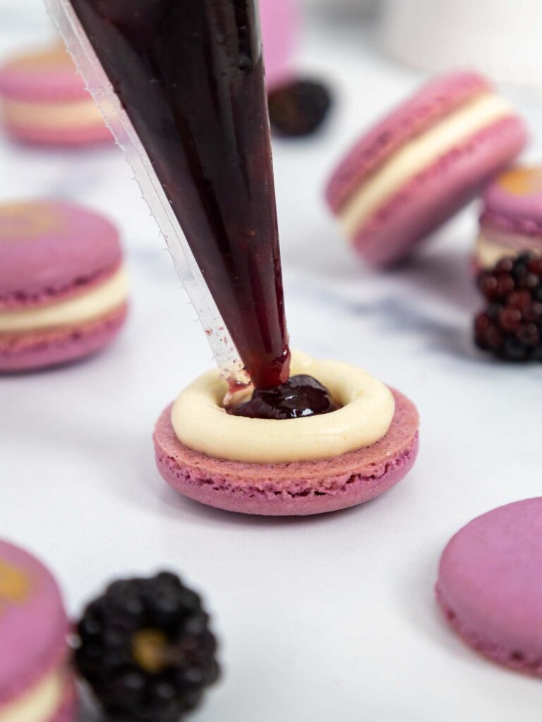 image of a blackberry macaron being filled with blackberry jam