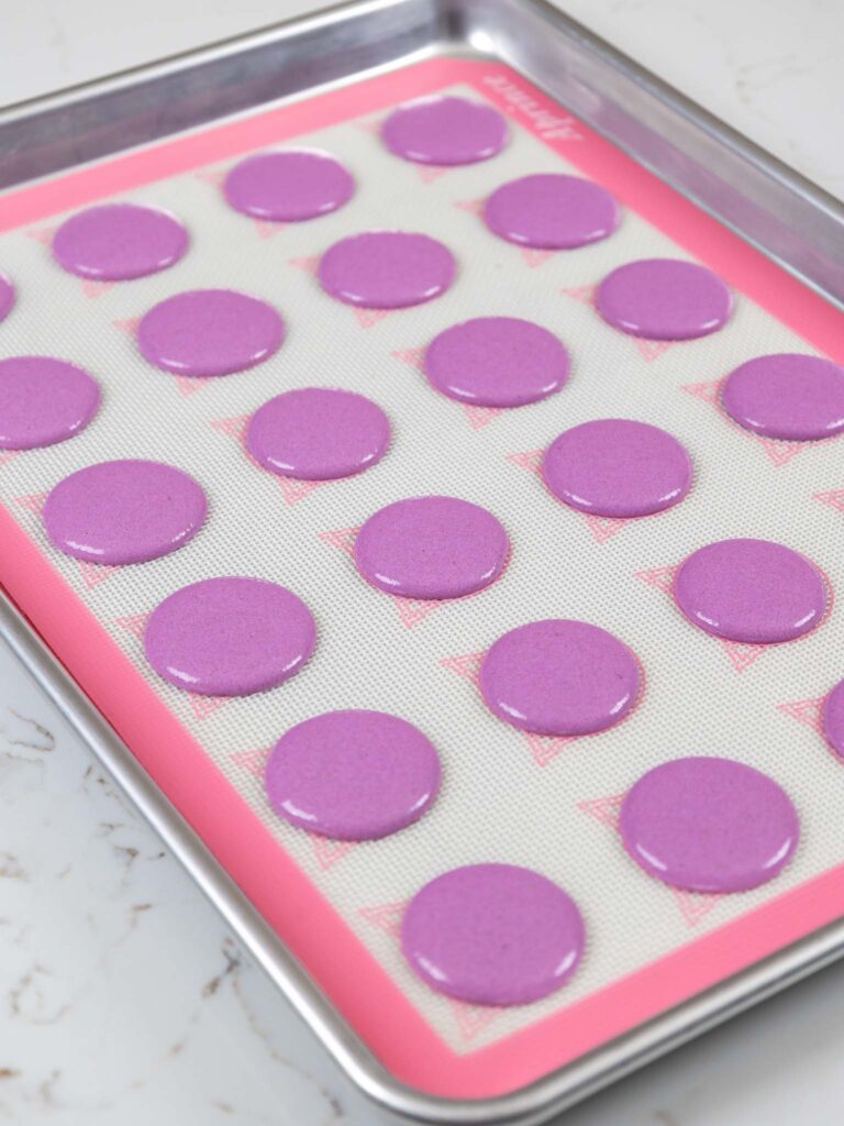 image of purple macaron shells that have been piped on a silpat mat and are resting before being baked