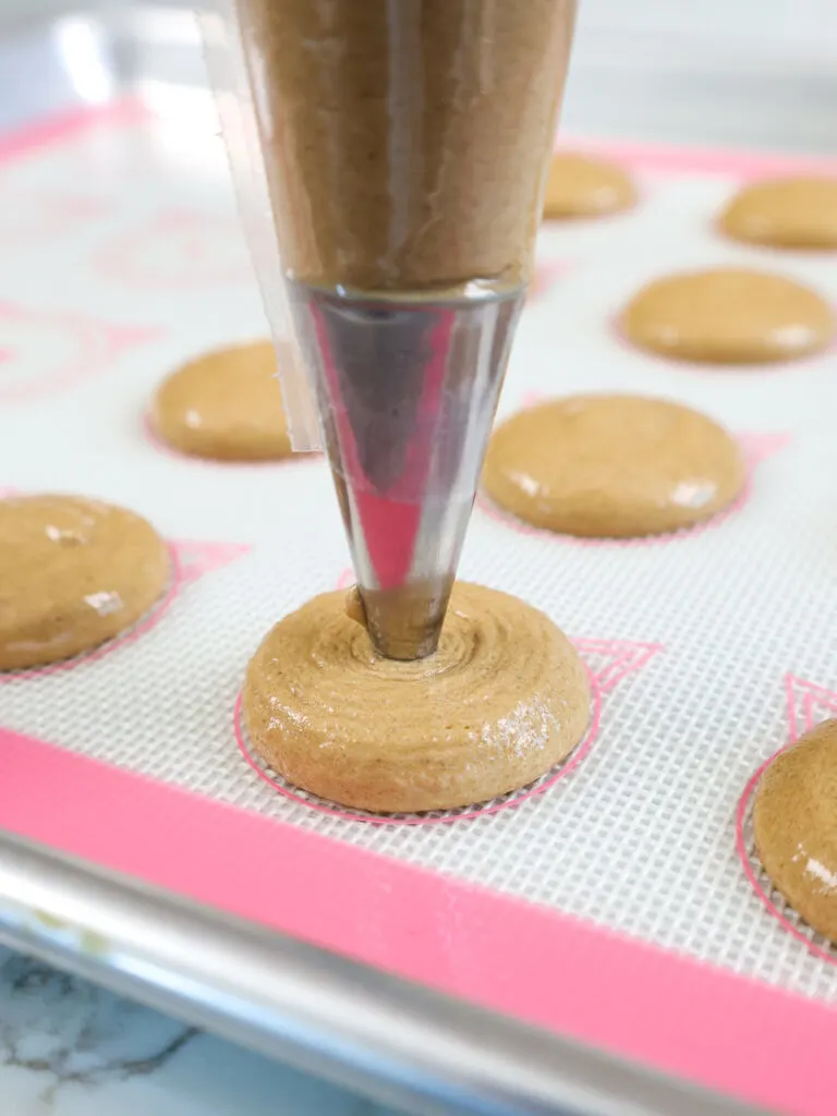 image of a chocolate macaron shell being piped onto a silpat mat