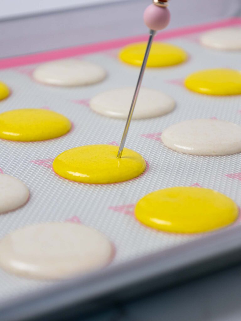 image of an air bubble being popped in a yellow macaron shell with a scribe