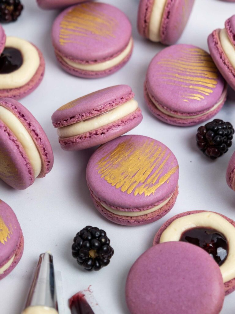 image of blackberry macarons that have been filled with blackberry jam and decorated with a brush of edible gold paint