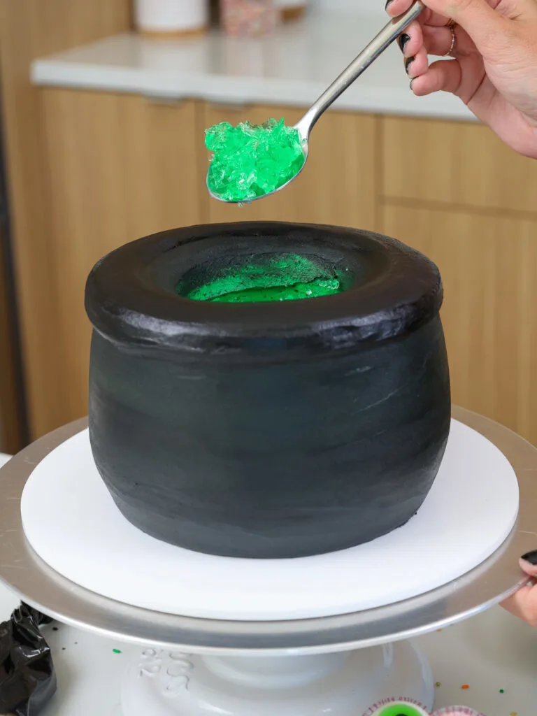 image of jelly crumbles being added into the center of cauldron cake to look like a potion