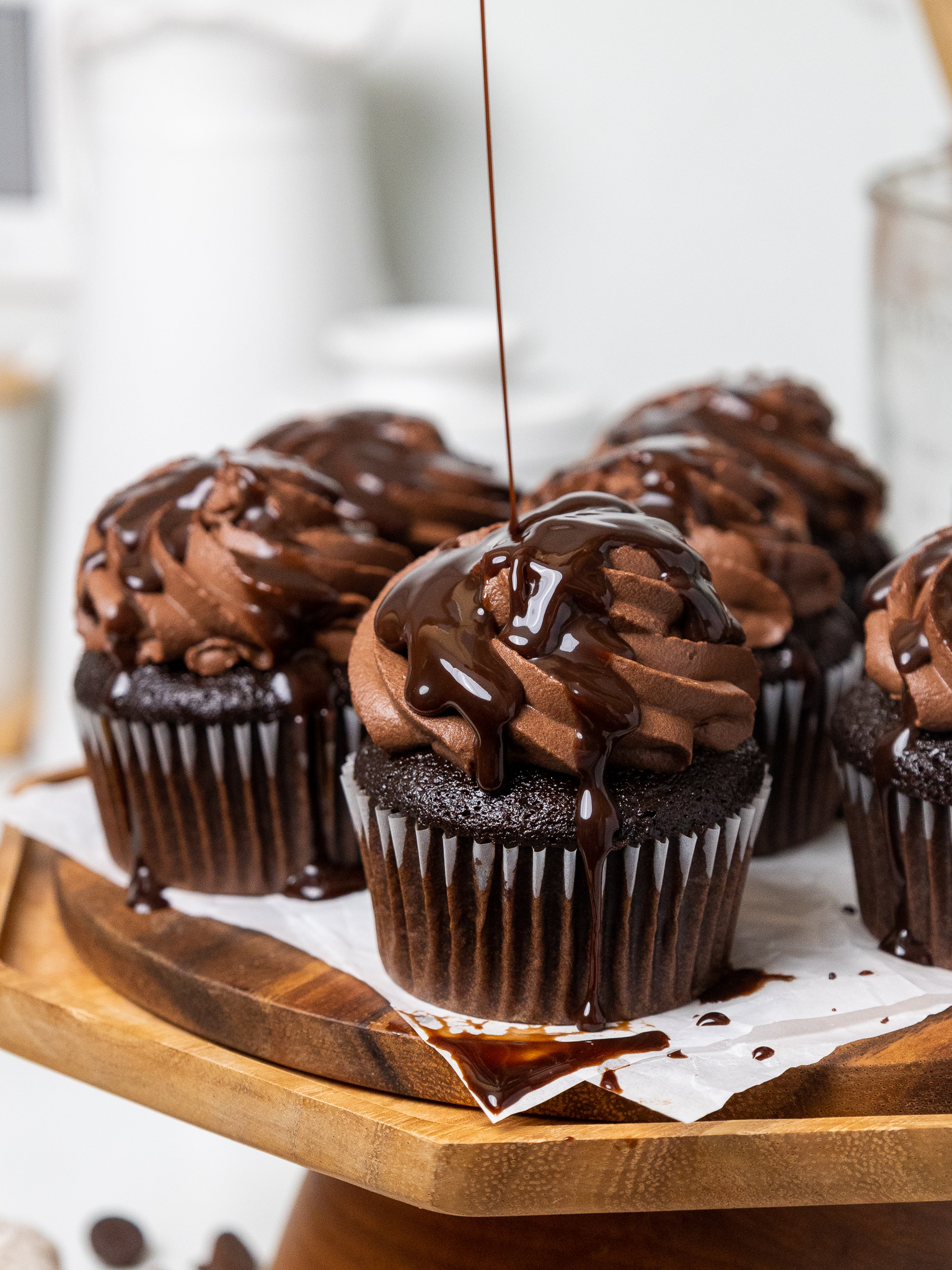 image of chocolate syrup being drizzled over chocolate whipped cream frosting on cupcakes