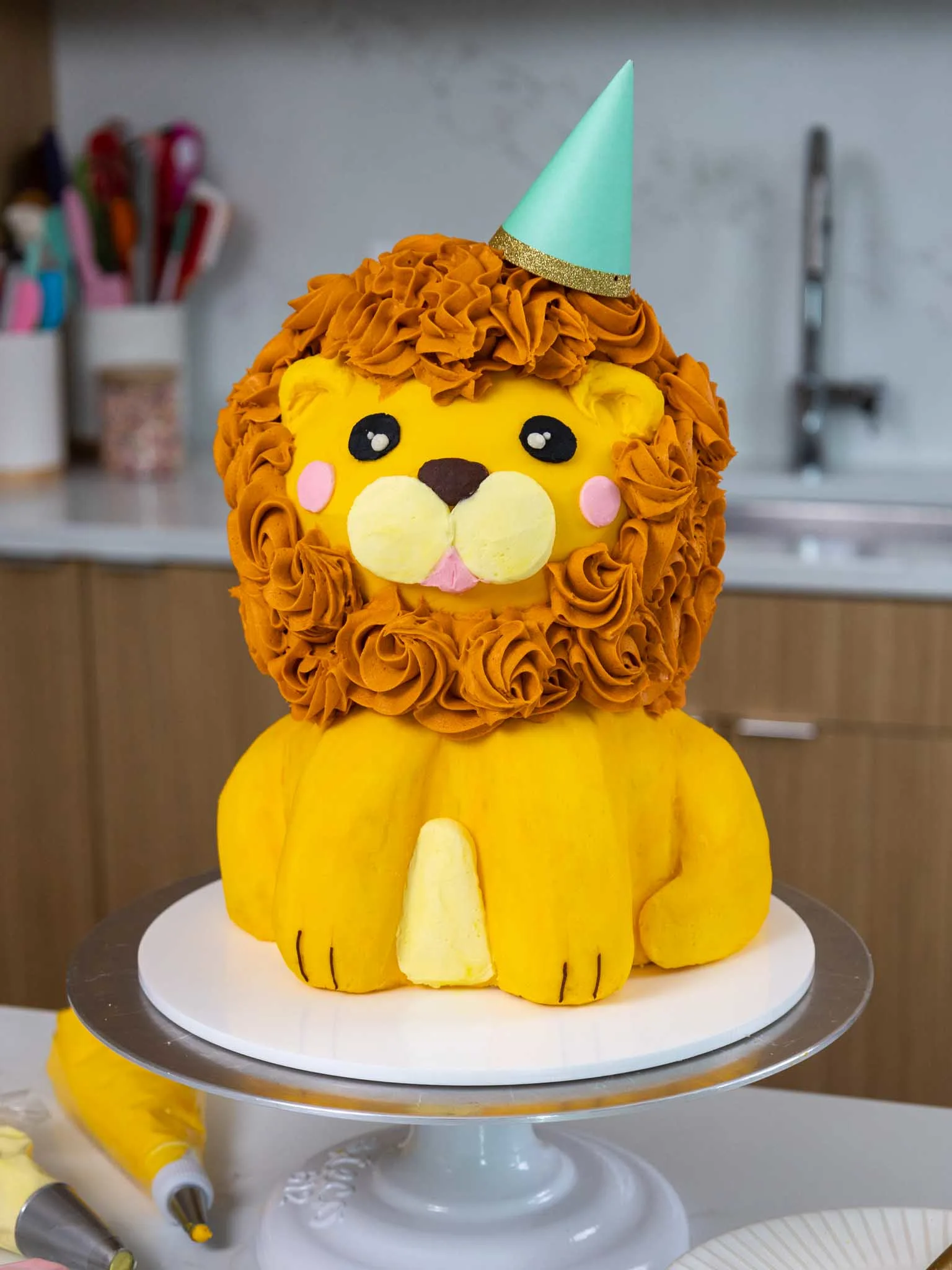 image of a cute buttercream lion cake that's wearing a party hat