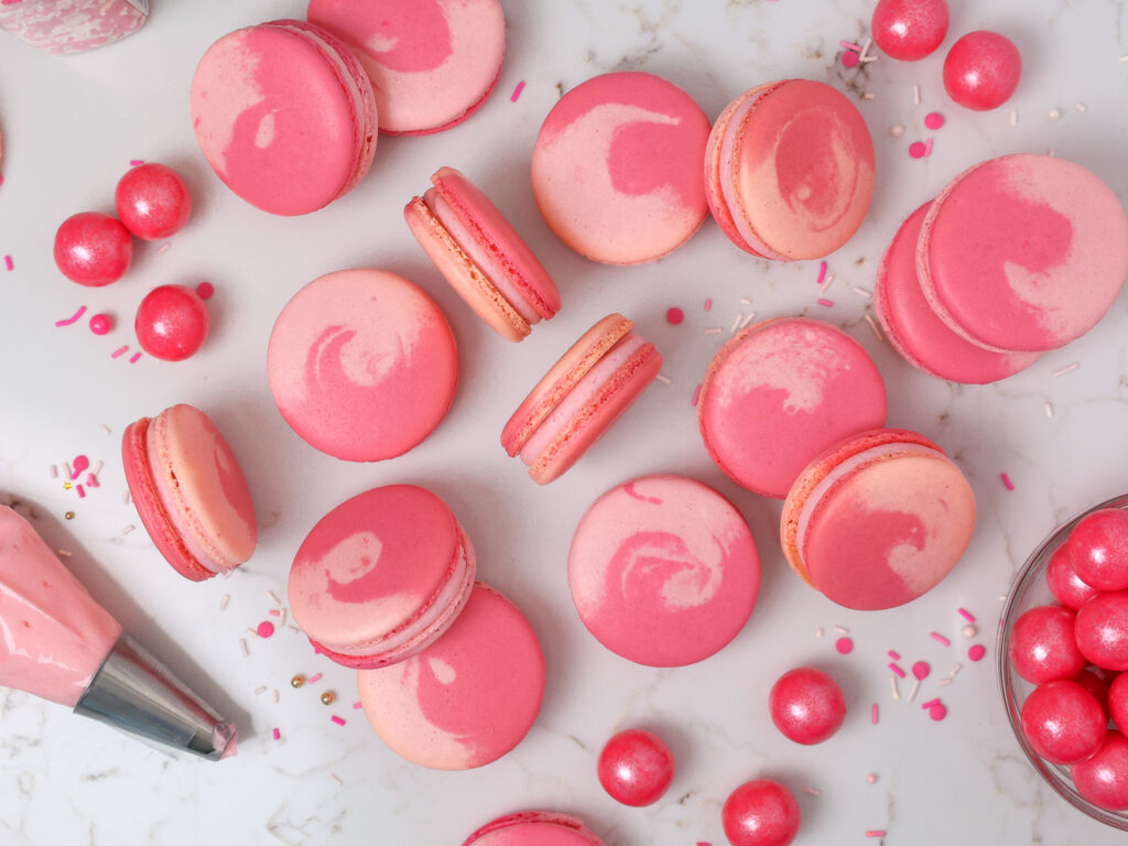 image of bubblegum macarons laid out on a counter to show their two toned pink shells and bubblegum frosting filling