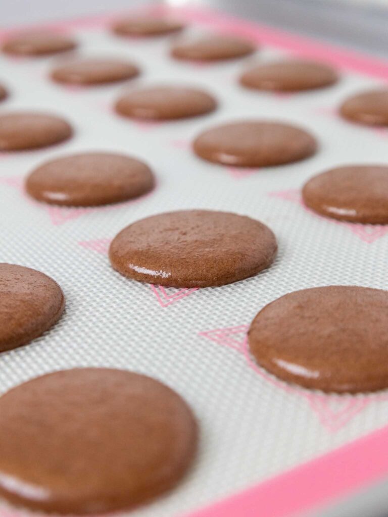 image of dark chocolate macaron shells that have been piped on a silpat mat