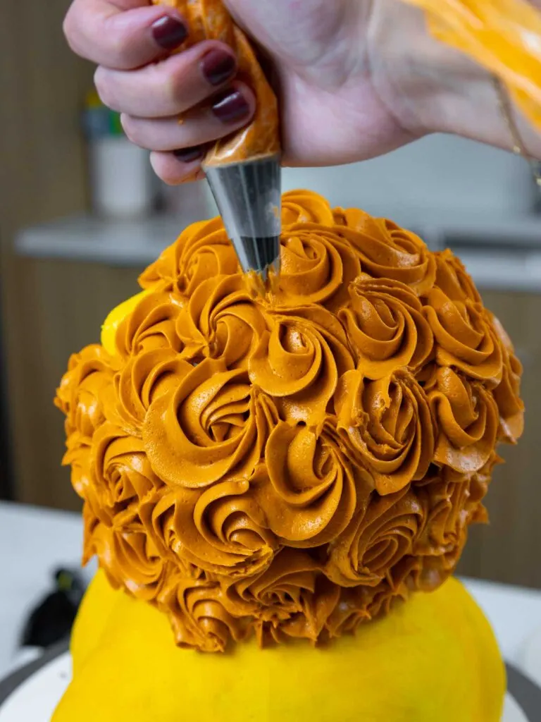 image of orange buttercream rosettes being piped onto a cake with a wilton 1M piping tip