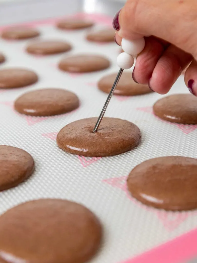 image of dark chocolate macaron shells that have been piped and are having small bubbles popped with a scribe
