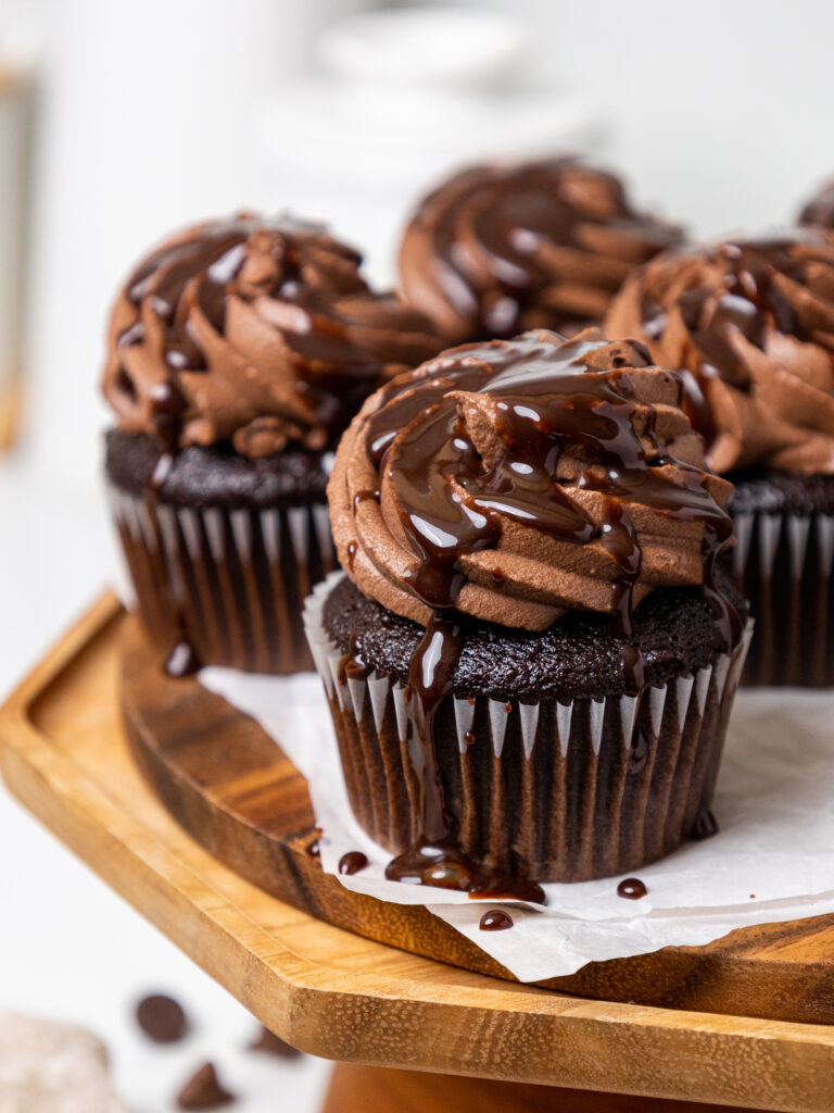 image of chocolate whipped cream frosting that's been piped on chocolate cupcakes and drizzled with chocolate syrup