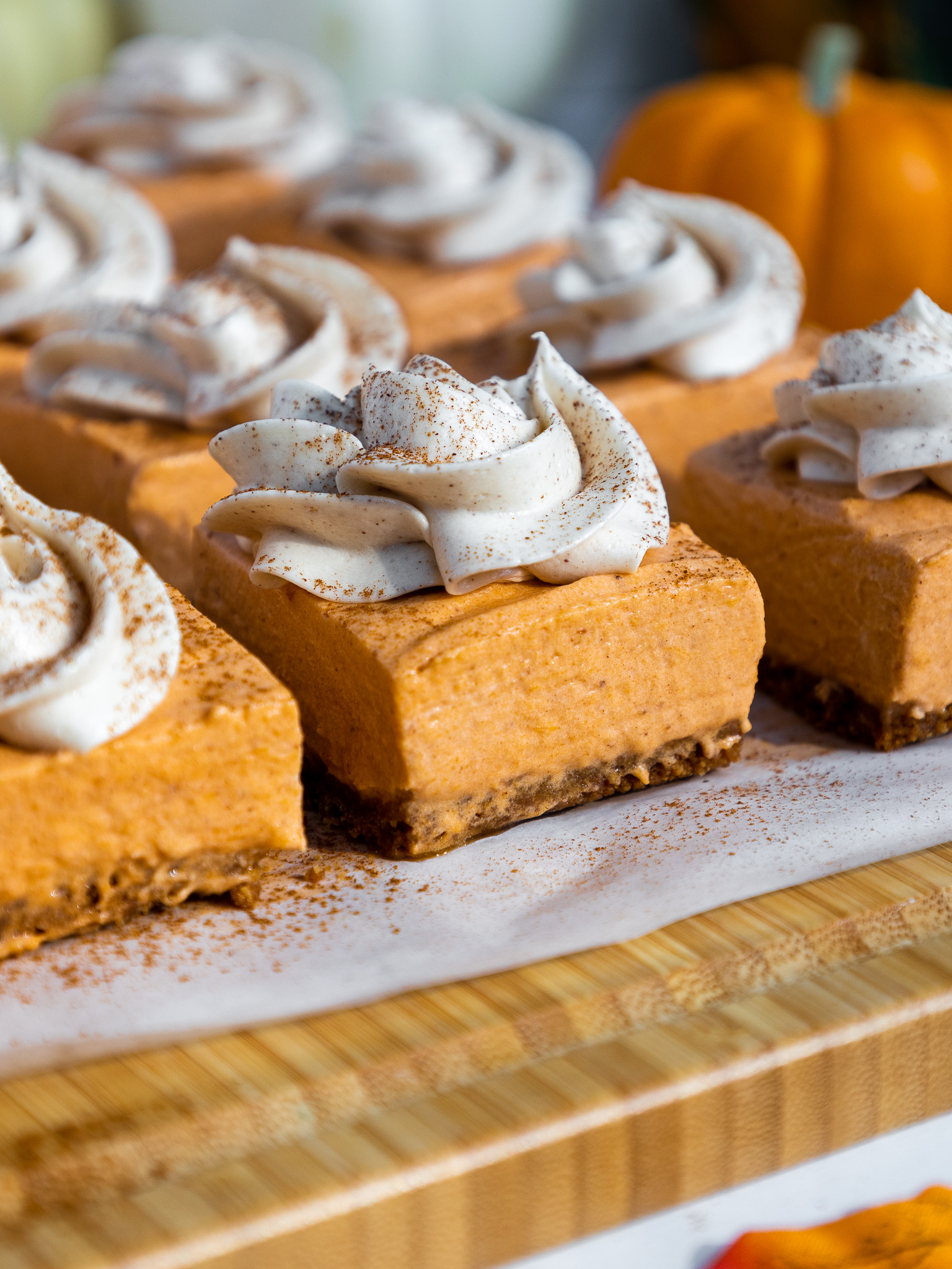 image of no bake pumpkin cheesecake bars that have been cut into squares and topped with whipped cream