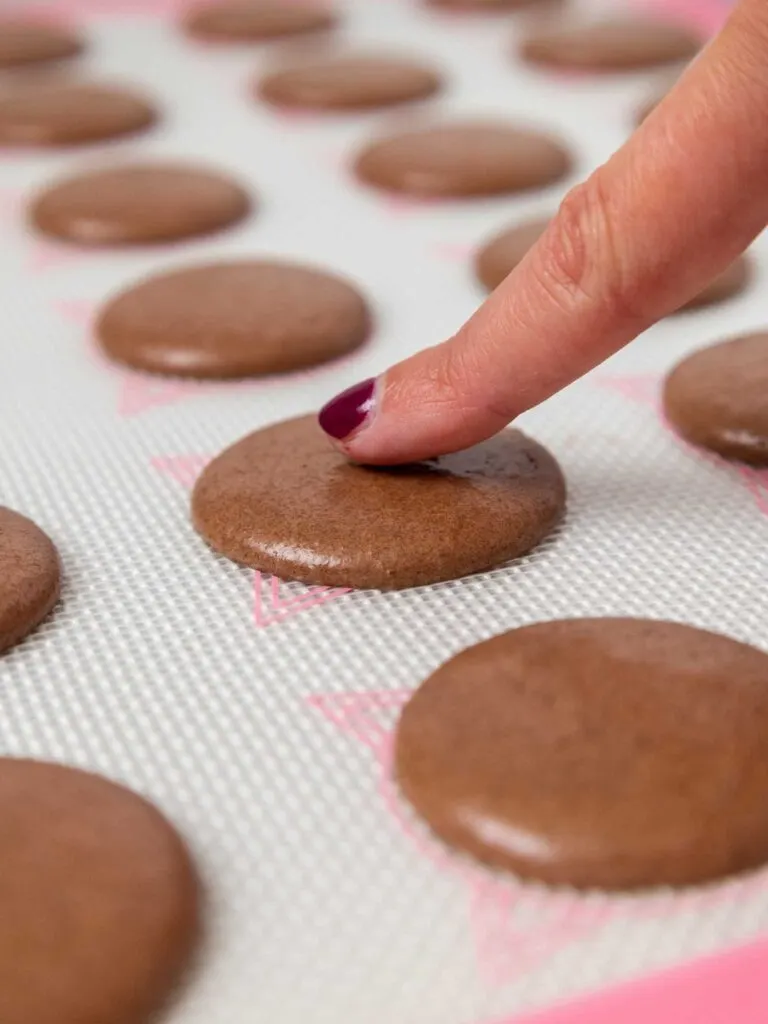 image of dark chocolate macaron shells that have been rested and have formed a skin