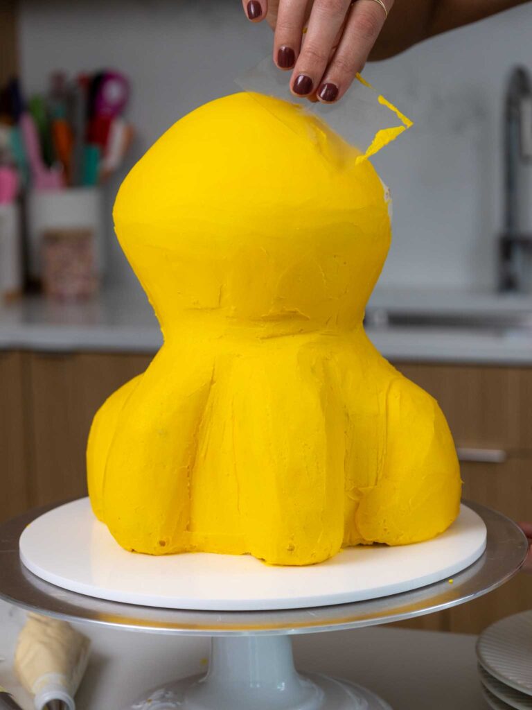 image of yellow buttercream being smoothed onto a cake using an acetate sheet