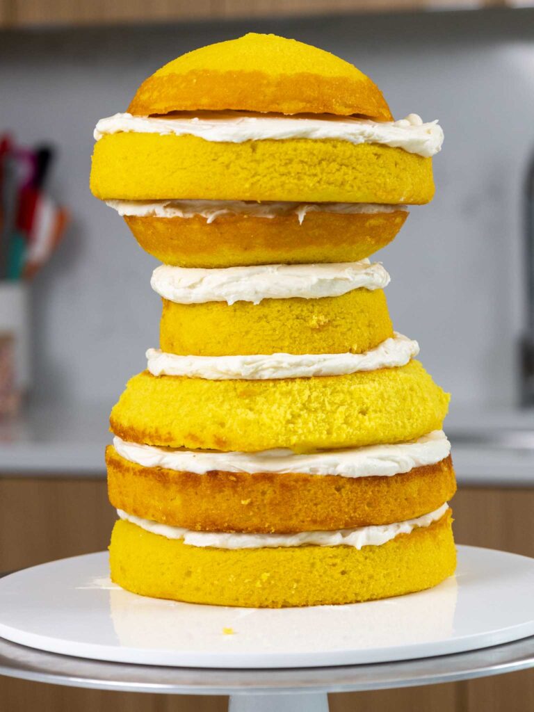 image of yellow cake layers being frosted and stacked on a cake board